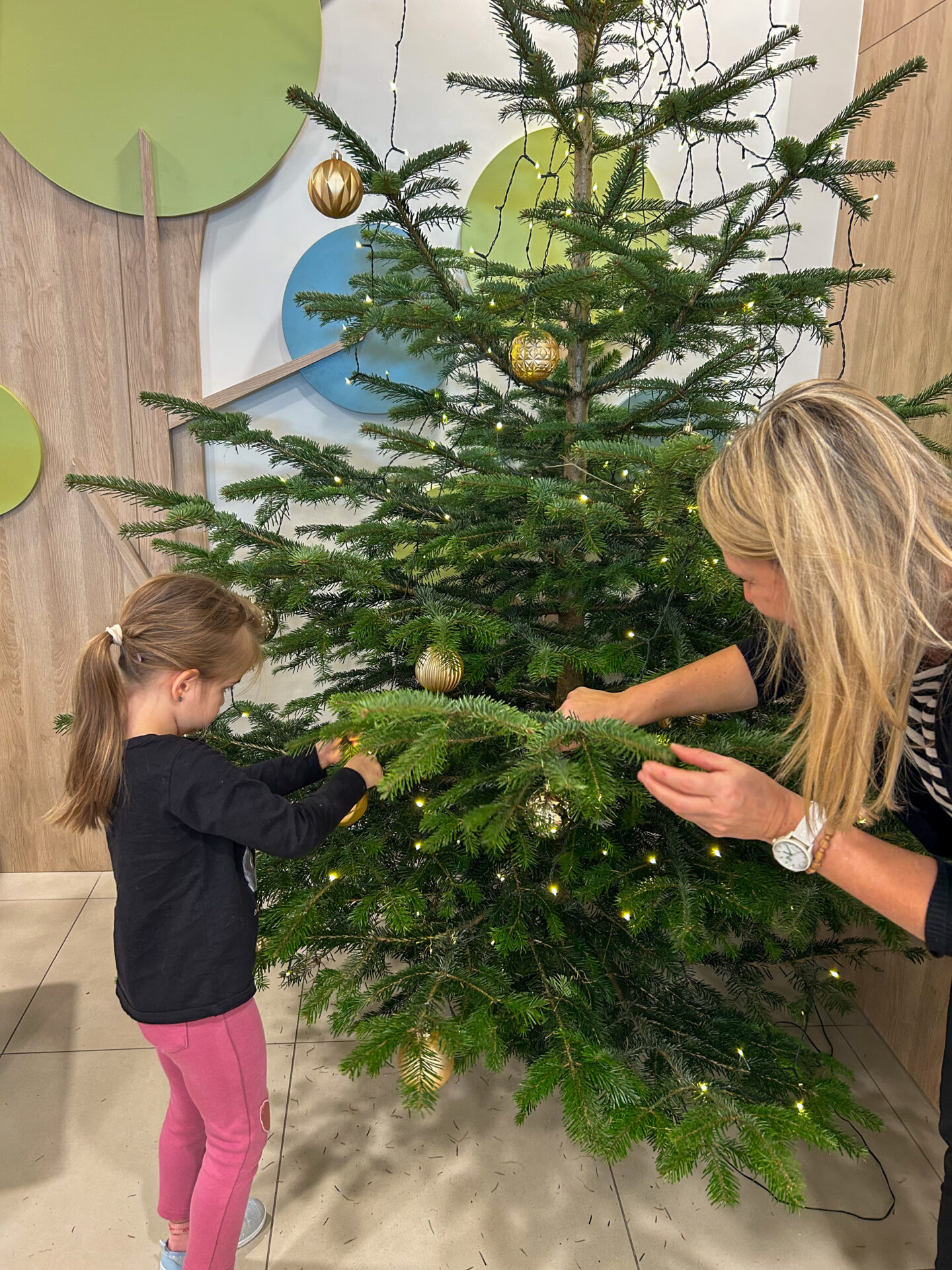 Kind und Mitarbeiterin schmücken den Christbaum Kind und Mitarbeiterin schmücken den Christbaum