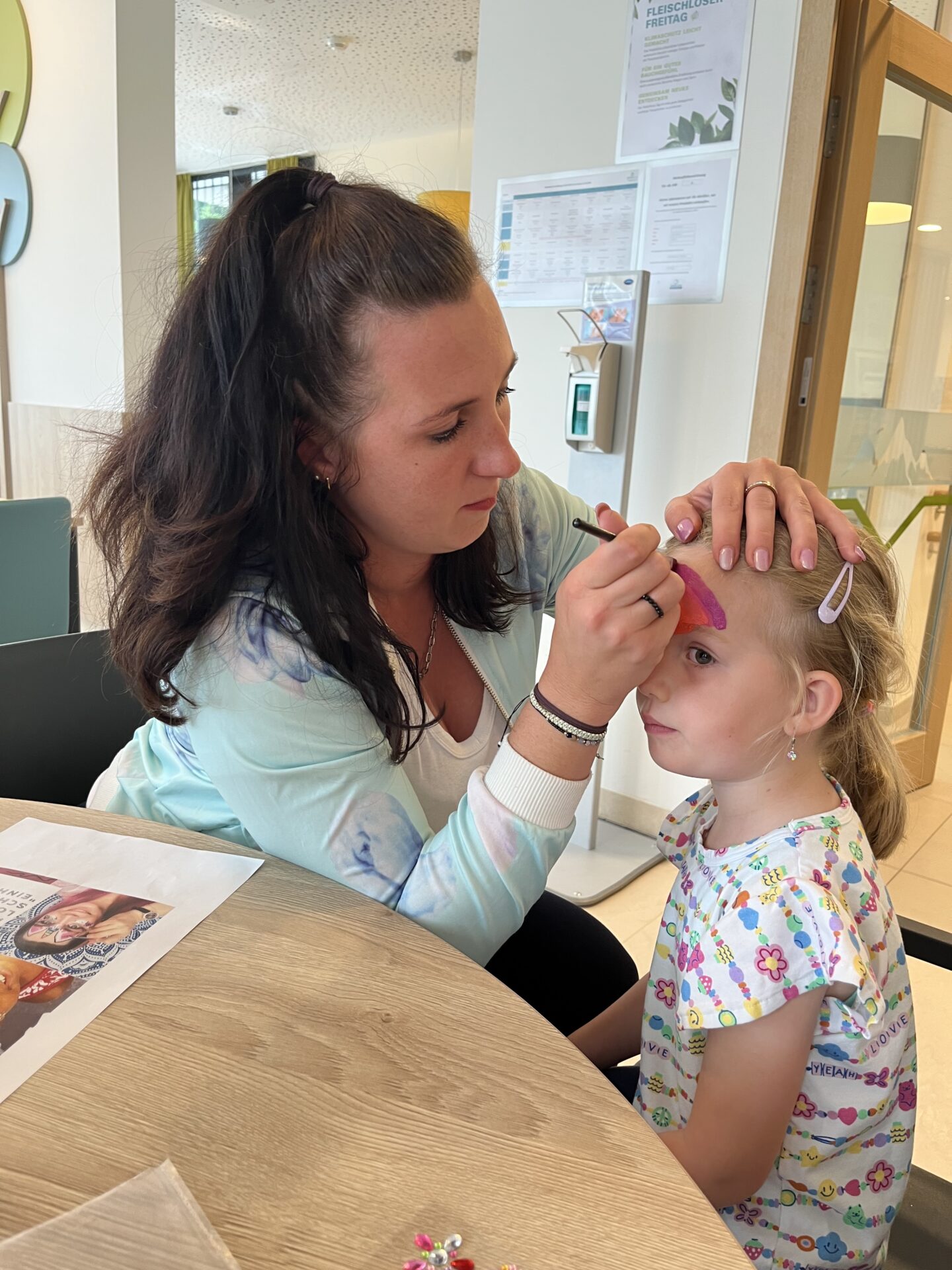 Mitarbeiterin der Rehaklinik schminkt ein Kind Mitarbeiterin der Rehaklinik schminkt ein Kind